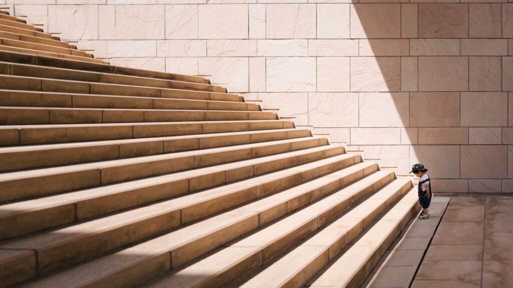 A kid looking up a flight of stairs showing the desire to go up, albeit baby steps. Just like the determination you need to accomplish your goals using micro goals. Success Through Failure episode 294: A Surprisingly Simple Trick To Staying On Track With Your Goals: A Power Tactic To Use Every Month