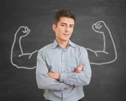 A man standing in front of a blackboard with a drawing of 2 arms flexing (Success Through Failure podcast episode #430 Ironclad Confidence: 12 Strategies for Unstoppable Success)