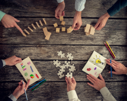People placing a bunch of things on a table: blocks, dominos, notebooks, pens (Success for the Athletic-Minded Man podcast episode #453 Systems to Simplify Your Life and Give You Back Your Time (and One System to Rule Them All)