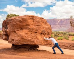 A woman tring to push a boulder (Success for the Athletic-Minded Man podcast episode: Beyond Hard Work: Embracing Inspired Action for Greatness)